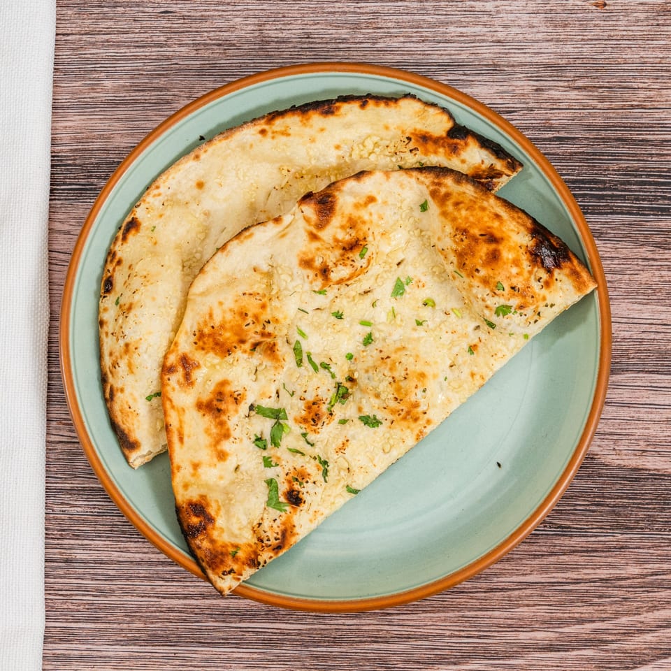 Two pieces of golden-brown Indian naan bread, garnished with herbs, on a light blue plate.